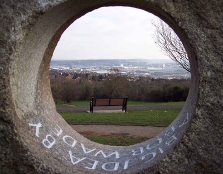 Inscription within the hole of a holed memorial stone that frames a view over Rochester